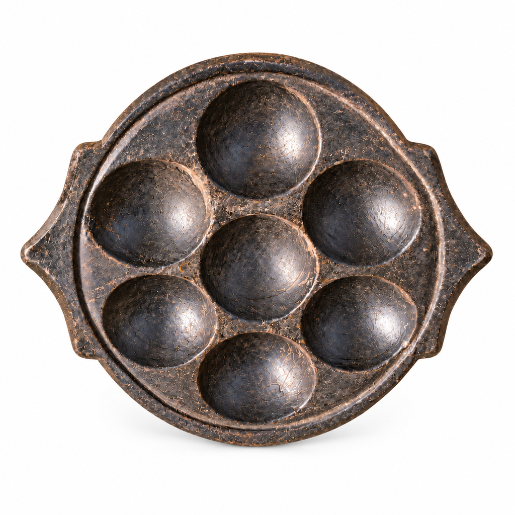 South-Indian-stone- idli-mould with seven rounded wells and pointed side handles on a white background
